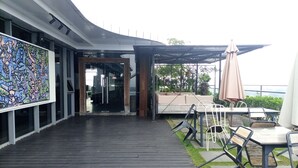 Ein Außenbereich mit einer Holzterrasse, Sitzgelegenheiten mit Tischen und Stühlen sowie ein großes, farbenfrohes Wandgemälde an der Gebäudefassade.