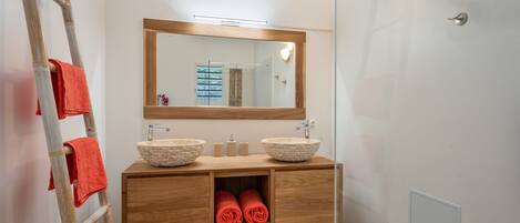 A bathroom with a wooden vanity, two vessel sinks, a mirror, and a towel rack.