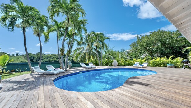 Eine Holzterrasse mit Schwimmbad, Palmen und Liegestühlen.