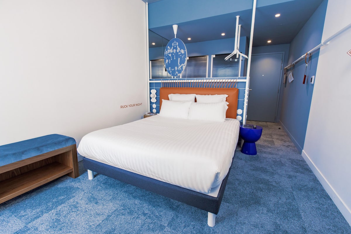 Een moderne slaapkamer met een bed, een bankje en een blauw tapijt.