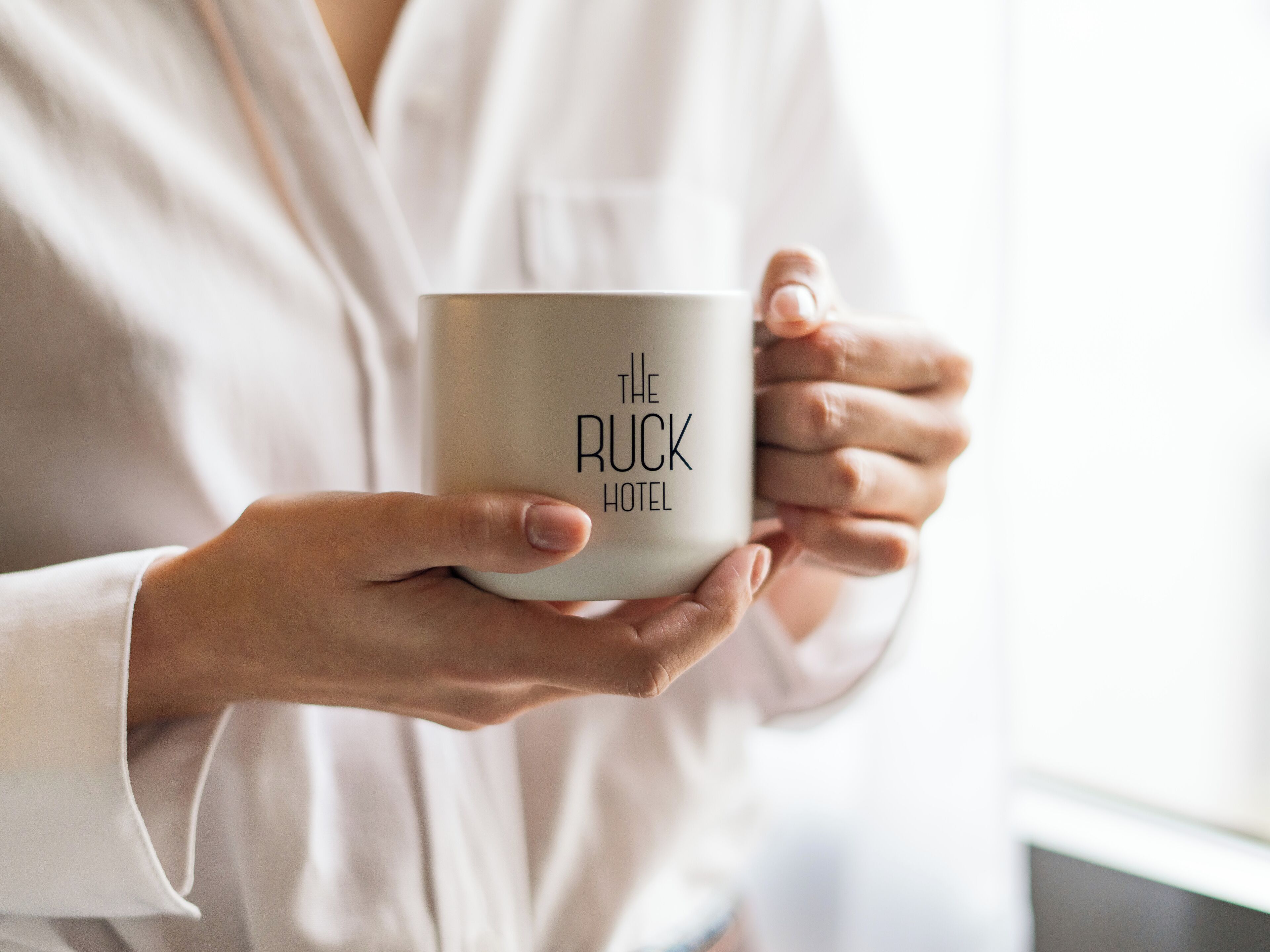 Una persona che tiene in mano una tazza con la scritta 'The Ruck Hotel'.