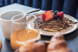 Un plato de postre con salsa de chocolate, fresas y frambuesas, acompañado de una taza de café y un vaso de zumo de naranja.