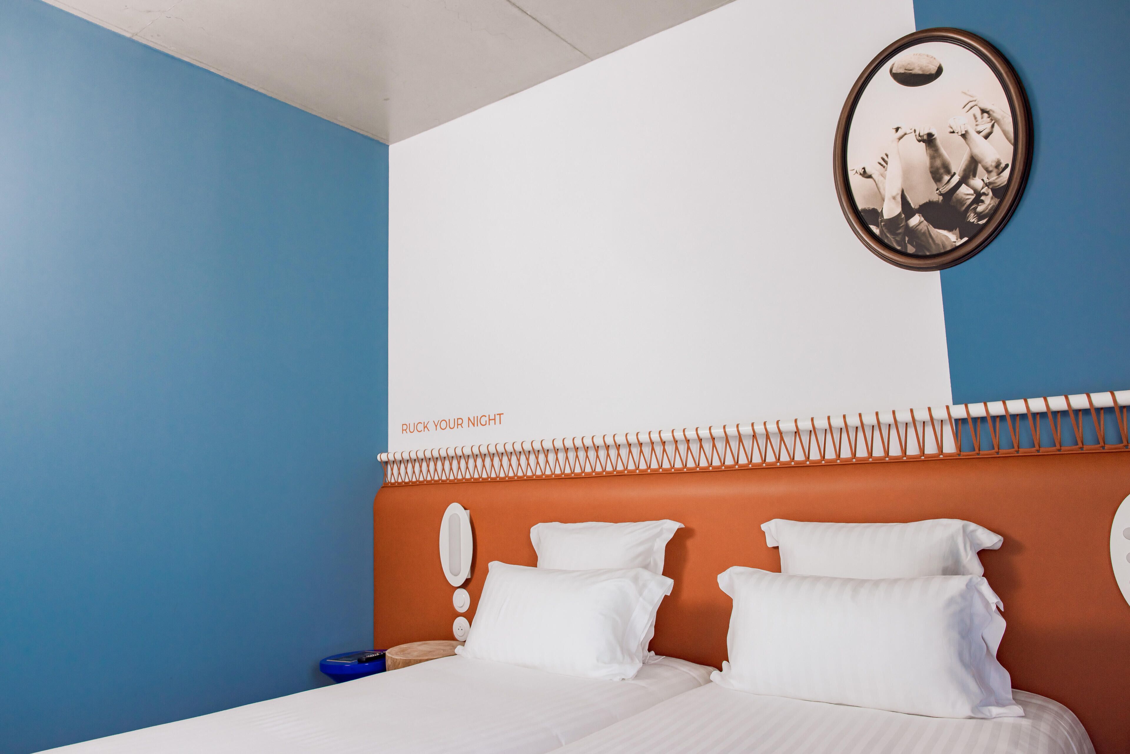 Ein Hotelzimmer mit Bett, weißen Kissen, einem Kopfende mit ungewöhnlichem Design und einem Wandbild.