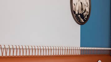 Habitación de hotel con una cama, almohadas blancas, un cabecero naranja y un espejo montado en la pared.