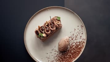 A dessert on a plate with a chocolate mousse and a scoop of ice cream, garnished with nuts and a leaf.