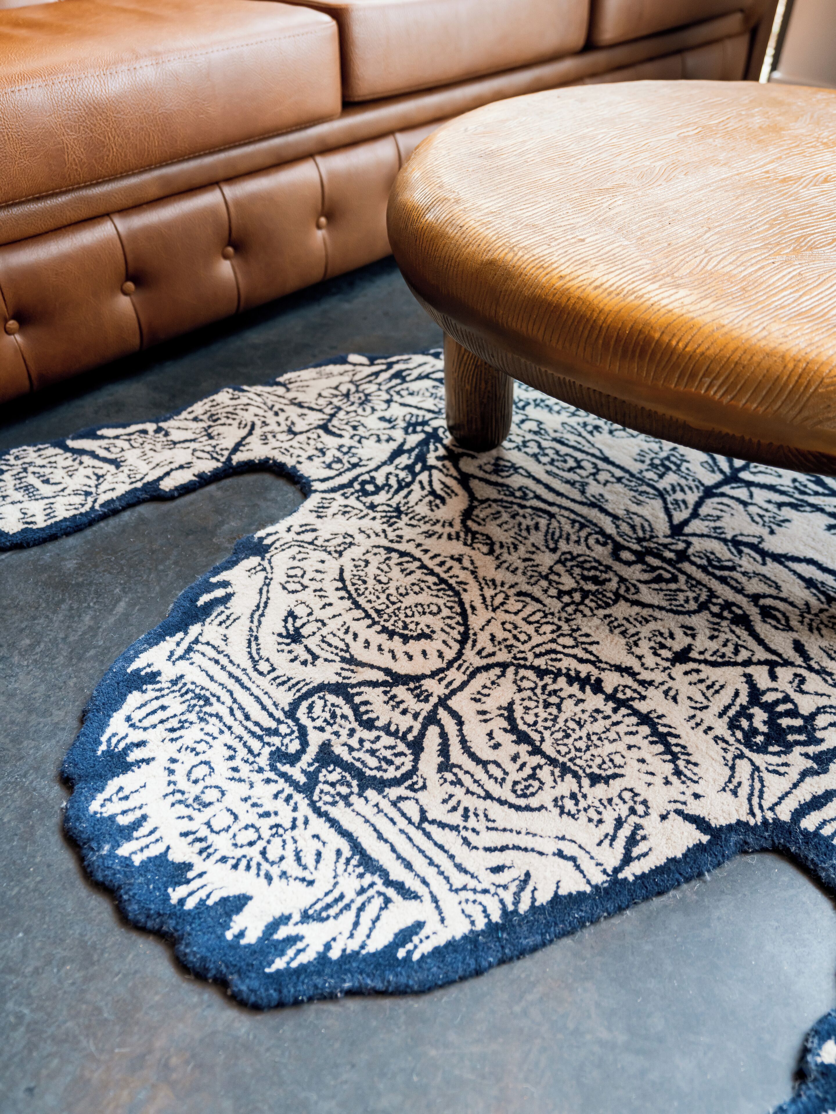 A patterned rug with a tufted ottoman and a leather sofa.