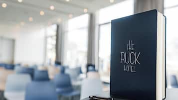 A black book titled "The Ruck Hotel" on a table in a hotel lobby with rows of chairs and large windows.