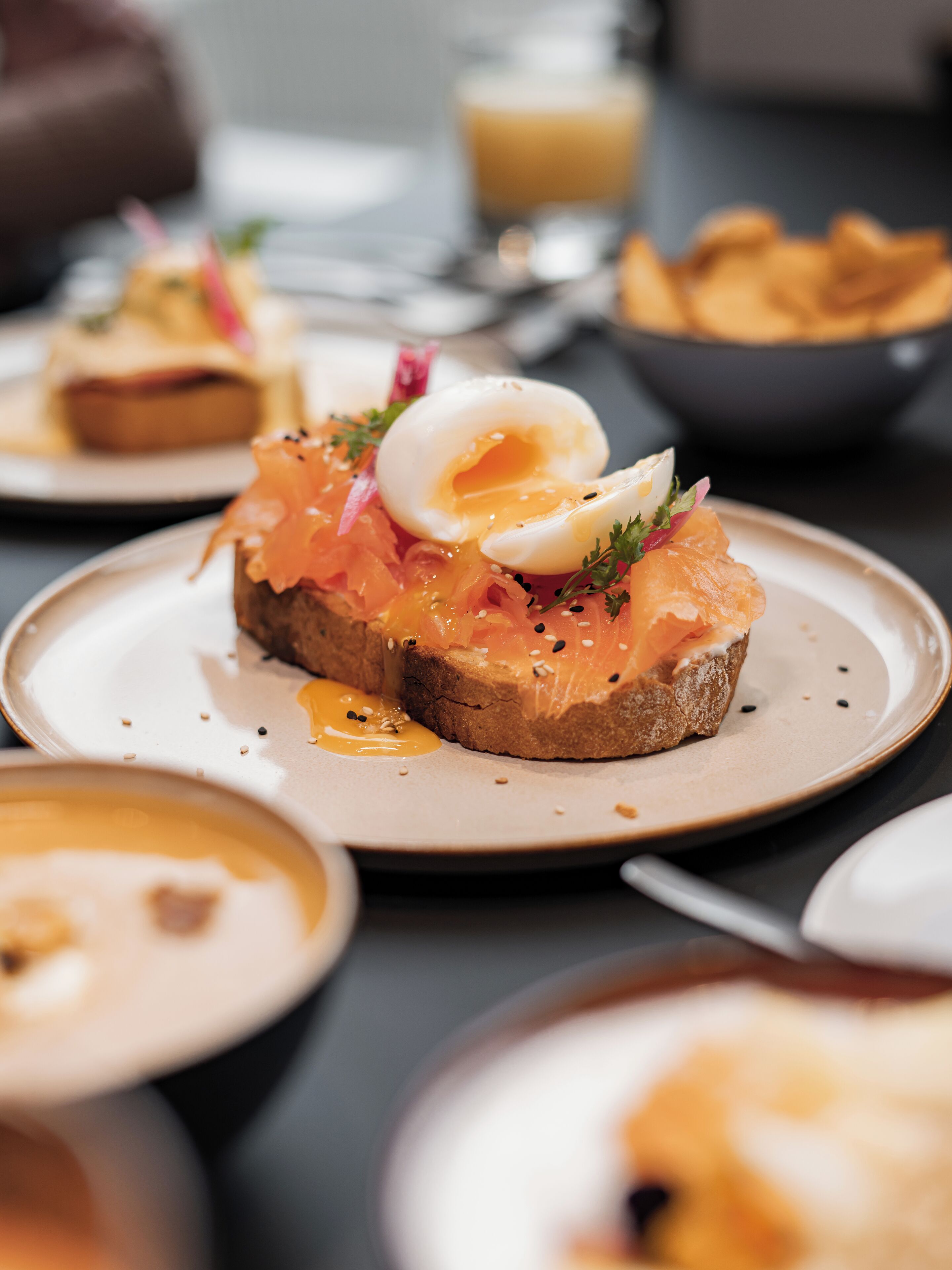 A breakfast setting with a plate of smoked salmon on toast, a poached egg, and garnishes.