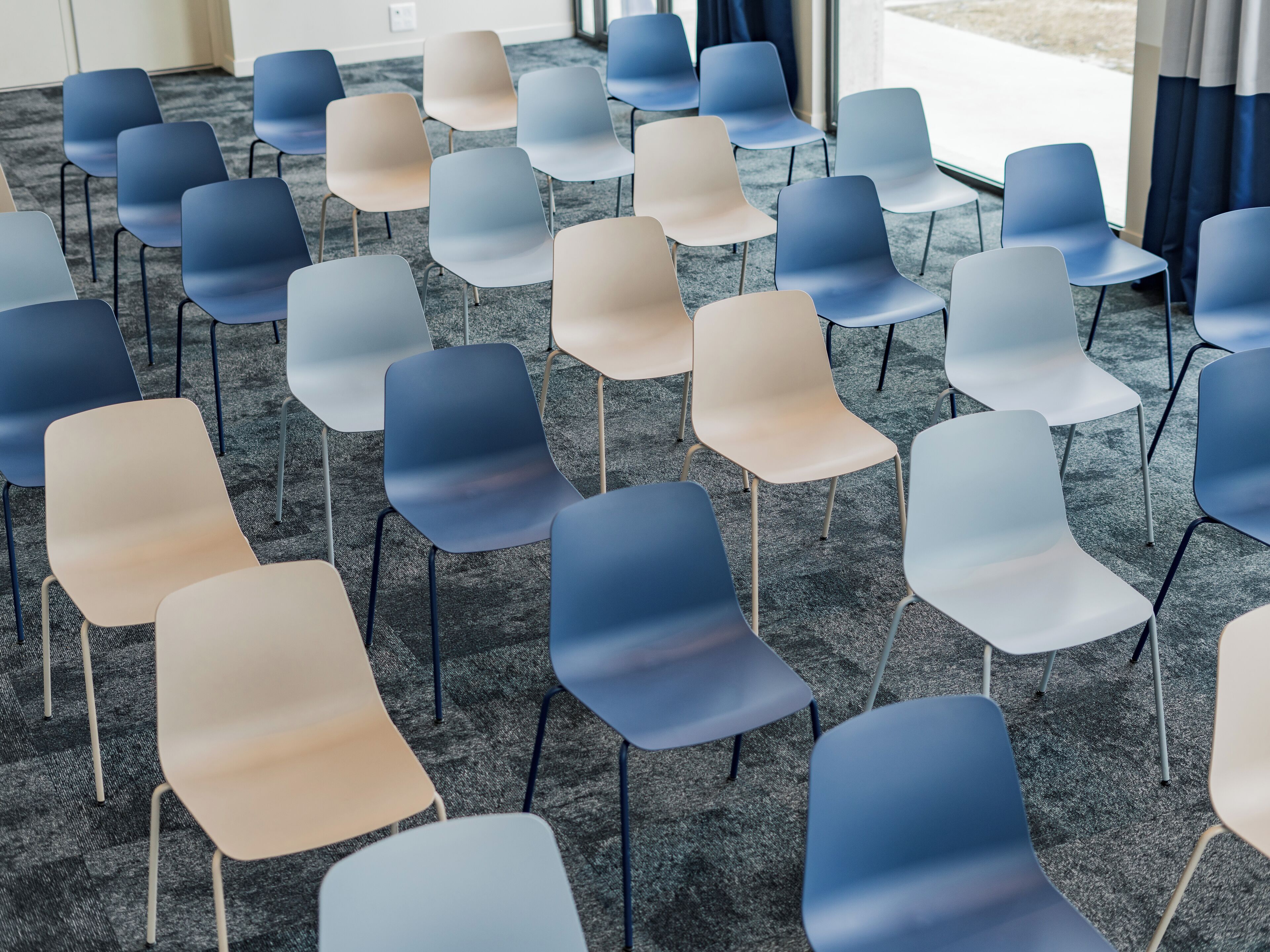 Rows of chairs arranged in a conference room with carpeted flooring and large windows.