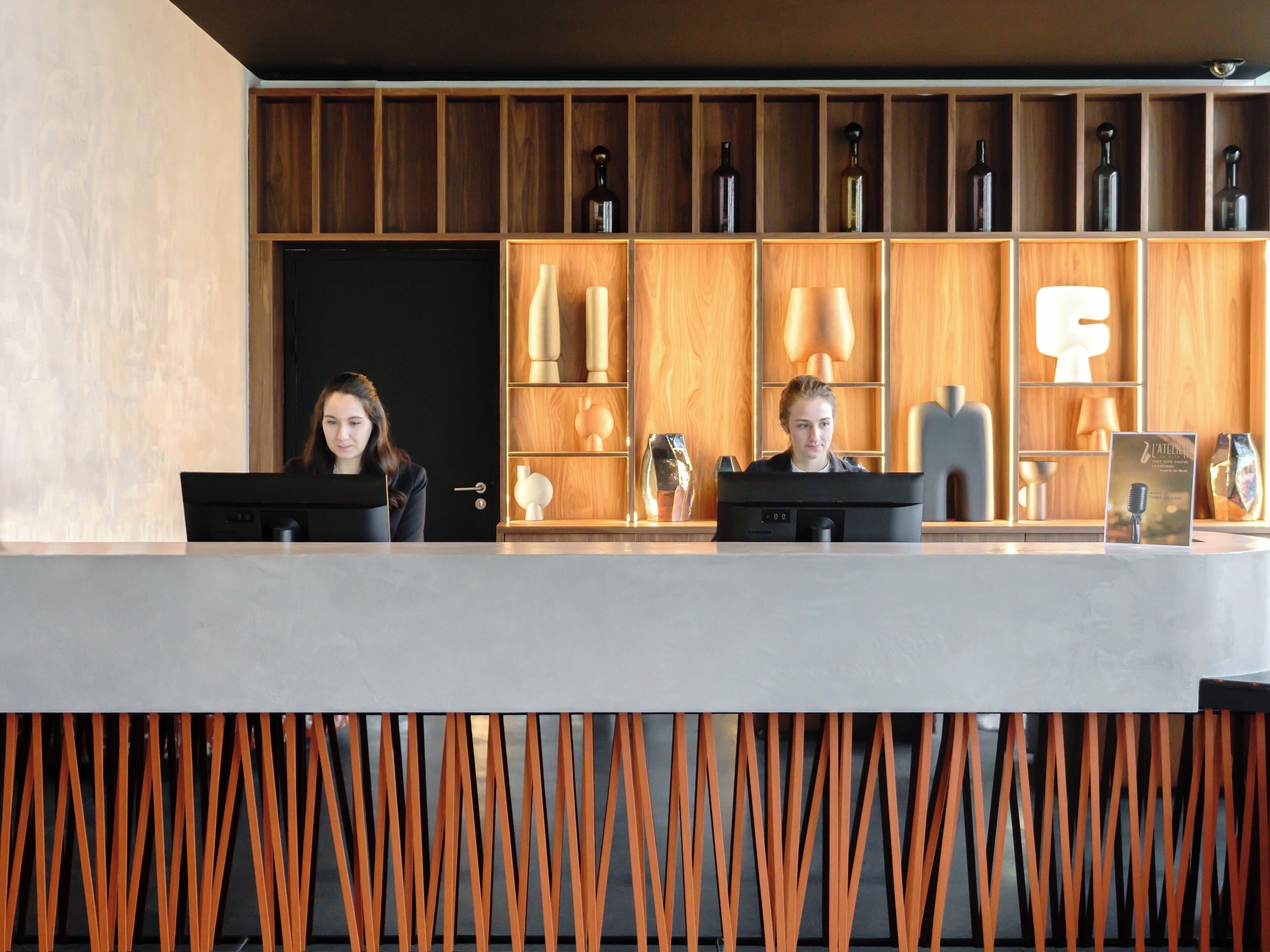 Una recepción con mostradores, dos empleados, estanterías de madera con adornos y un diseño interior moderno.
