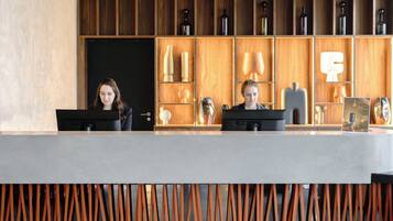 Een receptiebalie met twee medewerkers, houten planken met decoratieve objecten, en een modern interieur.