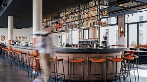 Zona de bar con mostrador, taburetes y estantes llenos de botellas.