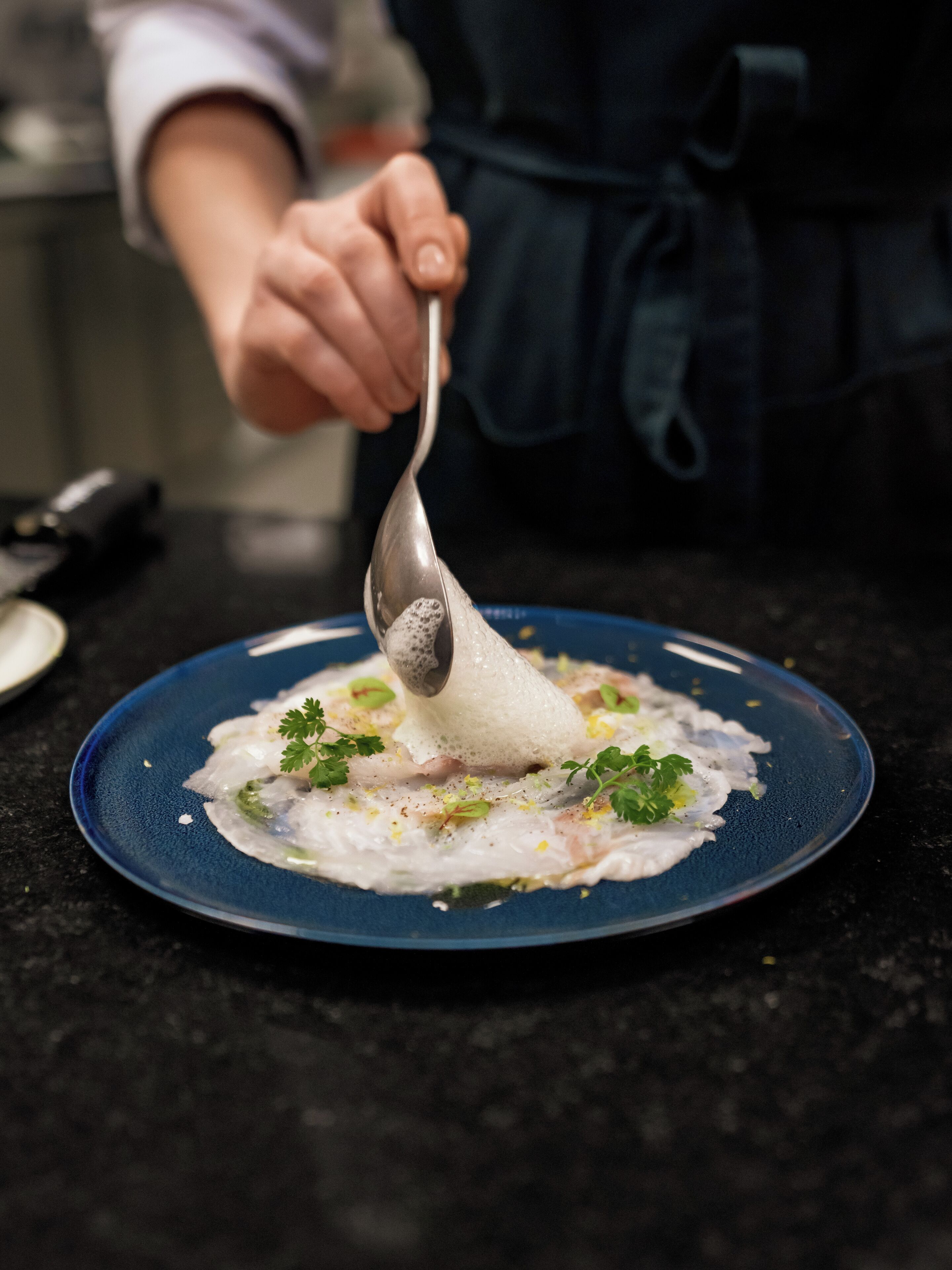 A person serving a dish on a blue plate with a spoon.