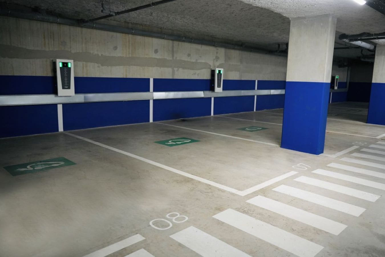 Een parkeergarage met blauwe en witte pilaren, groene parkeerplaatsen voor gehandicapten en witte parkeerlijnen.