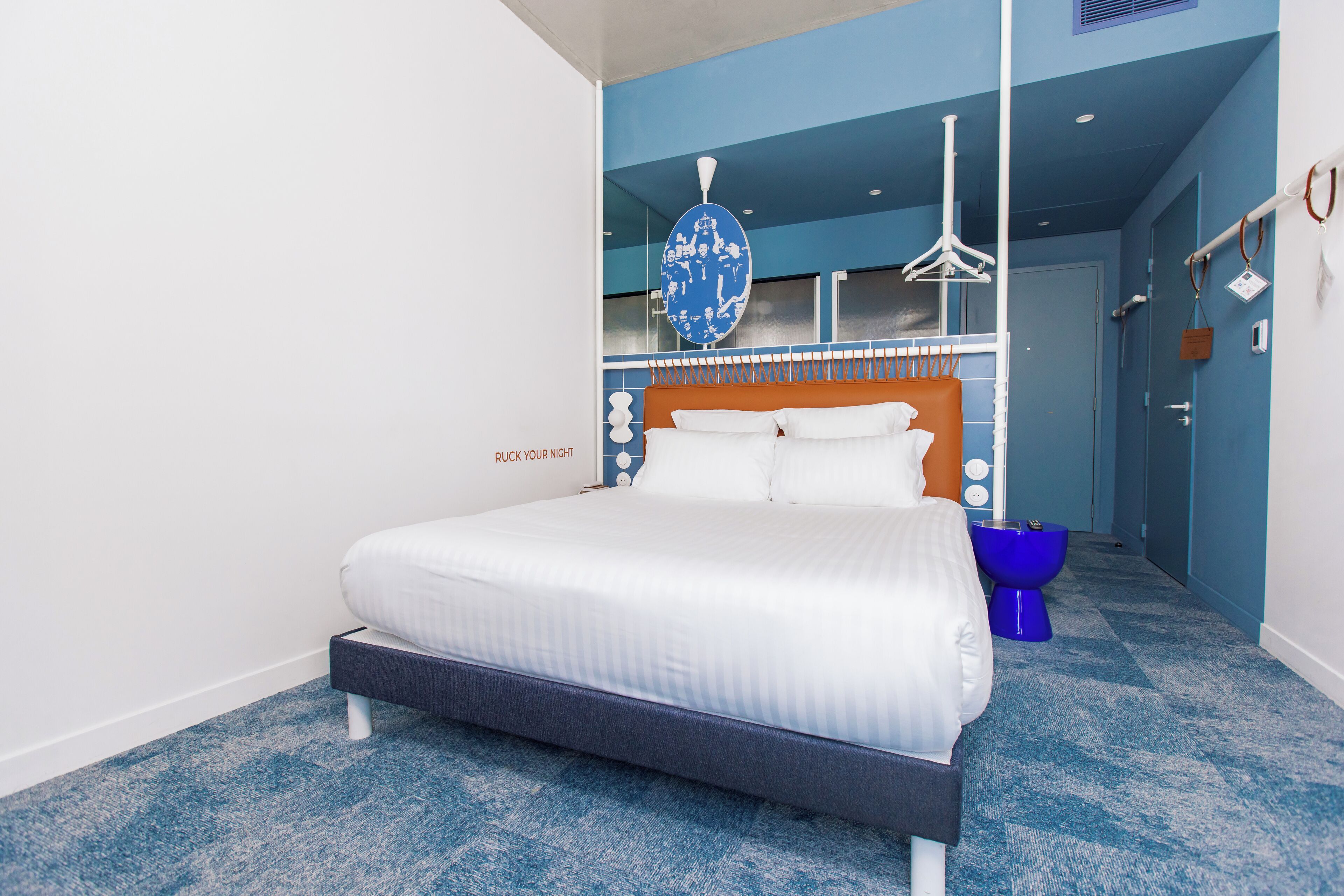 A modern hotel room with a large bed, a blue and white wall, and a blue carpet.