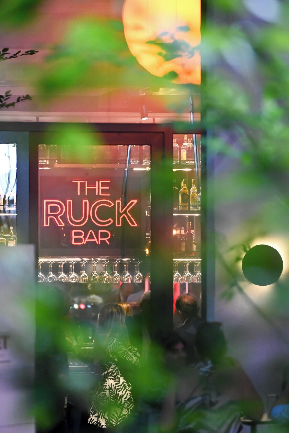A bar with a neon sign reading "The Ruck Bar" and shelves of bottles.