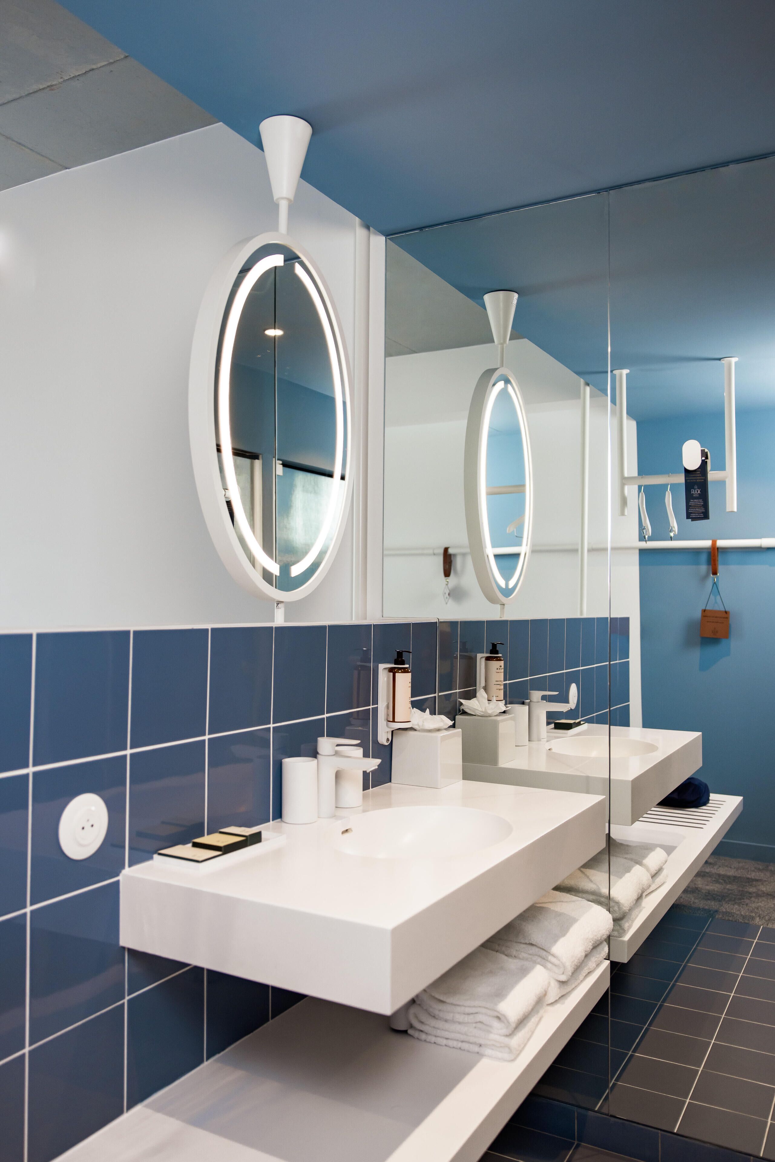 A modern bathroom with two sinks, a large mirror, and blue-tiled walls.