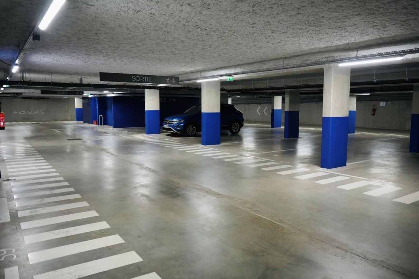 A multi-level underground parking garage with blue and white pillars, clear directional signage, and marked parking spaces.