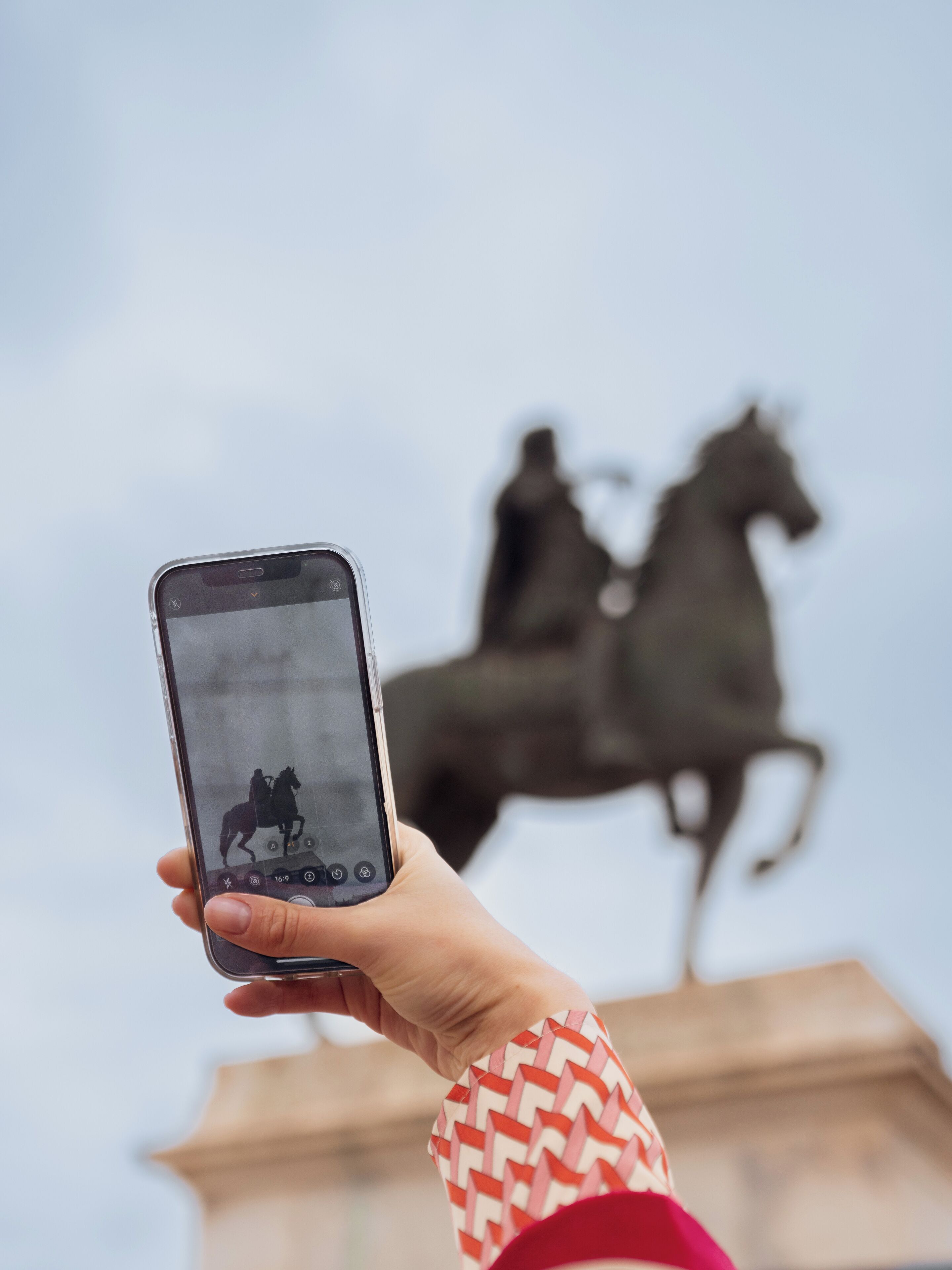 A hand holding a smartphone with a photo of a statue of a person on a horse.