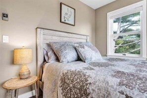 A bedroom with a bed, a bedside lamp, a window, and a framed picture on the wall.