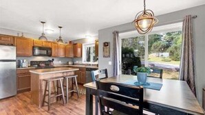 A kitchen with wooden cabinets, a bar stool, a dining table with chairs, and a hanging light fixture.