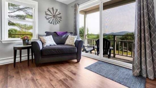 A living room with a dark sofa, a small table, and a large window with a view of greenery.