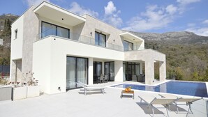 Ein modernes, zweistöckiges Haus mit Pool, großen Fenstern und einer Bergkulisse.