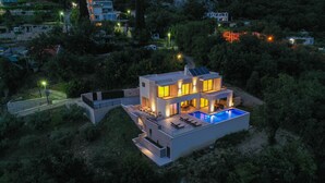 Ein modernes, zweistöckiges Haus mit Swimmingpool, umgeben von Bäumen und Hügeln.
