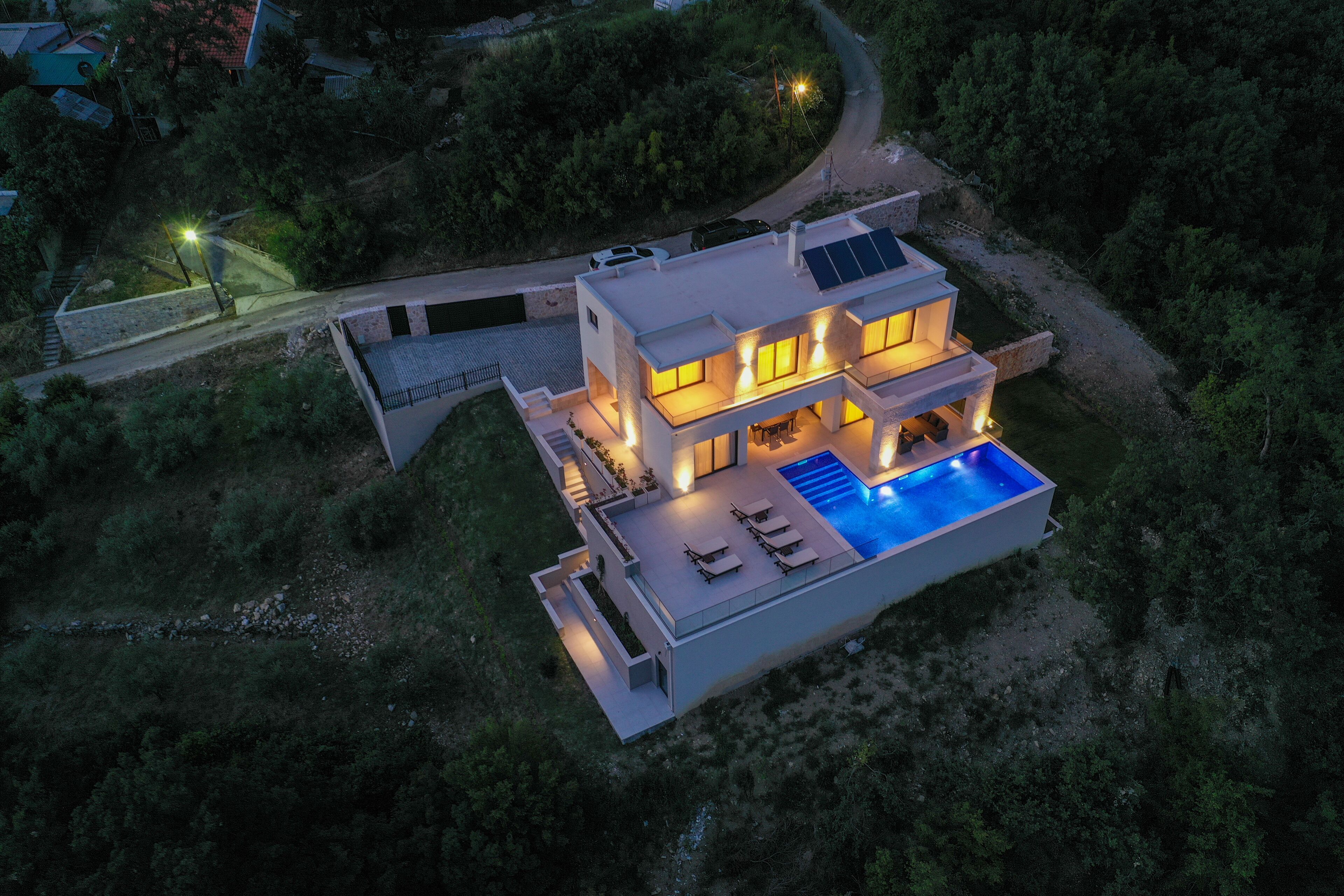 Una casa moderna de dos pisos con piscina, paneles solares e iluminación exterior.