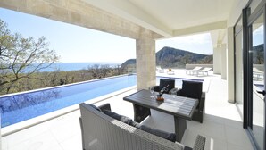 Eine Dachterrasse mit Pool, Gartenmöbeln und Blick auf das Meer und die Berge.