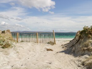 Una playa arenosa con una valla de madera que da al mar, rodeada de dunas y vegetación.