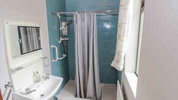 A bathroom with a sink, mirror, shower, and a window with a curtain.