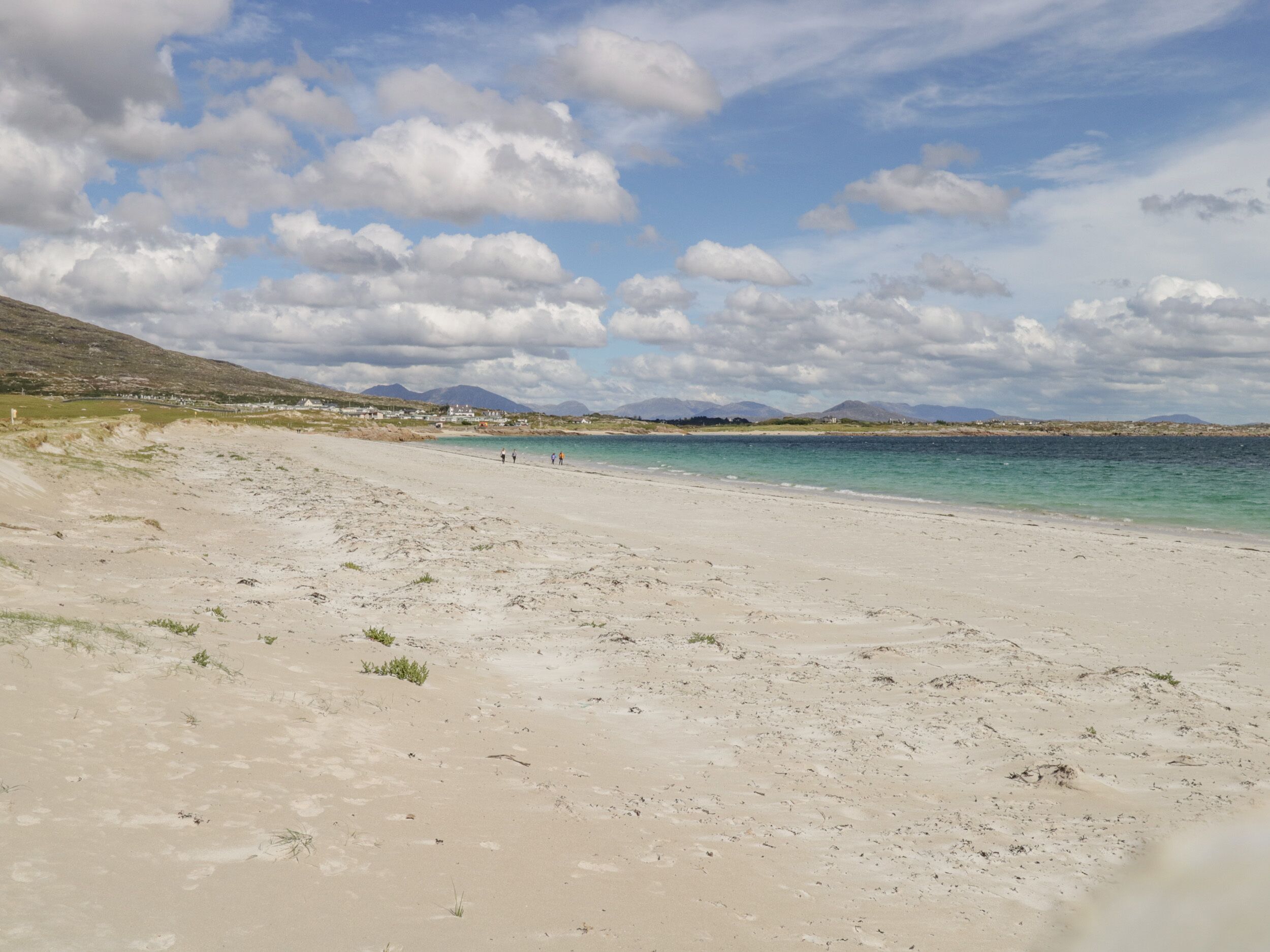 Une vaste plage de sable fin, sous un ciel dégagé, avec des montagnes qui se dessinent à l'horizon.