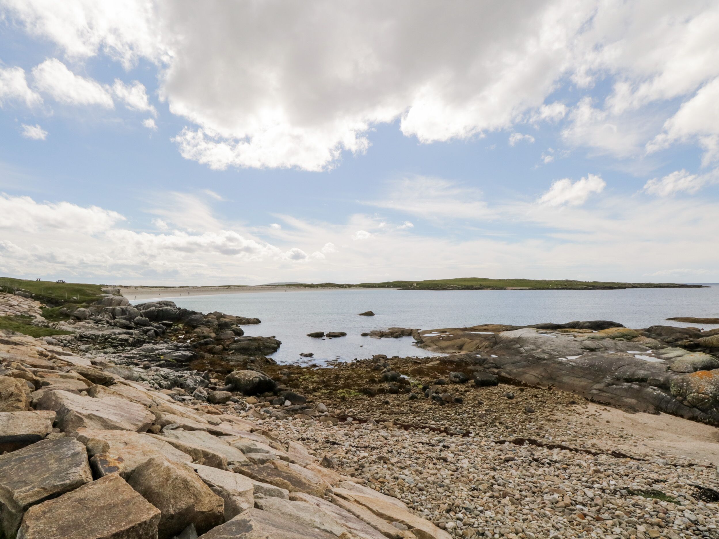 A rocky shoreline with a view of the sea and distant hills.
