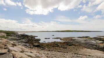 A rocky shoreline with a view of the sea and distant hills.