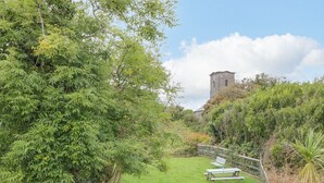 A lush garden with a stone wall, a picnic table, and a tower in the background.