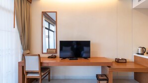 A modern hotel room with a wooden desk, a flat-screen TV, a chair, a small side table, and a window with curtains. - Sea Sand Sun Hua Hin by JC Kevin Hotel & Resort (Cha-am)