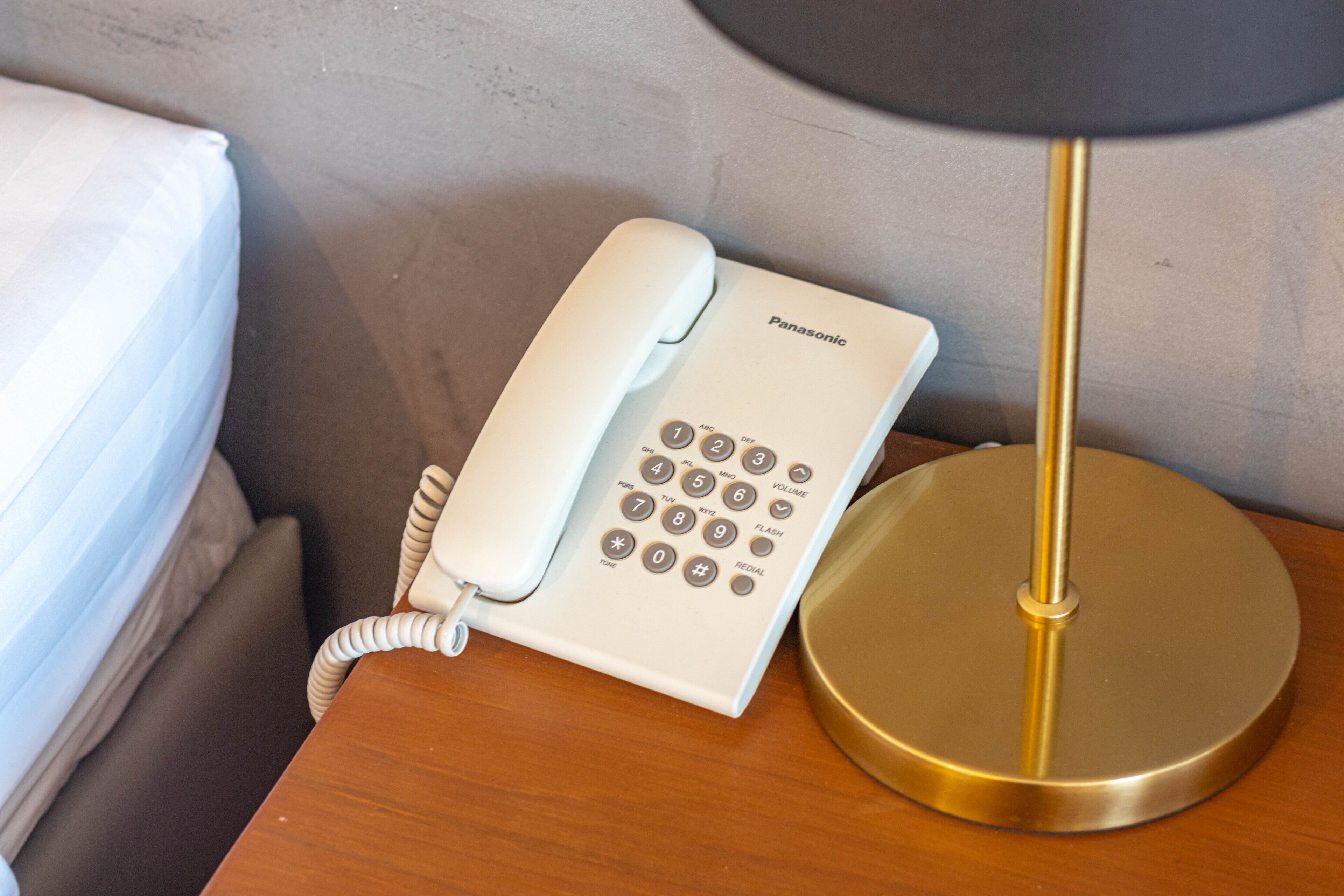 A white Panasonic telephone on a wooden bedside table next to a bed.