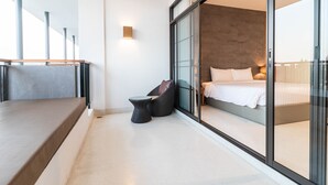A modern hotel room with a large sliding glass door leading to a balcony, a bed with white linens, and a small round table. - Sea Sand Sun Hua Hin by JC Kevin Hotel & Resort (Cha-am)