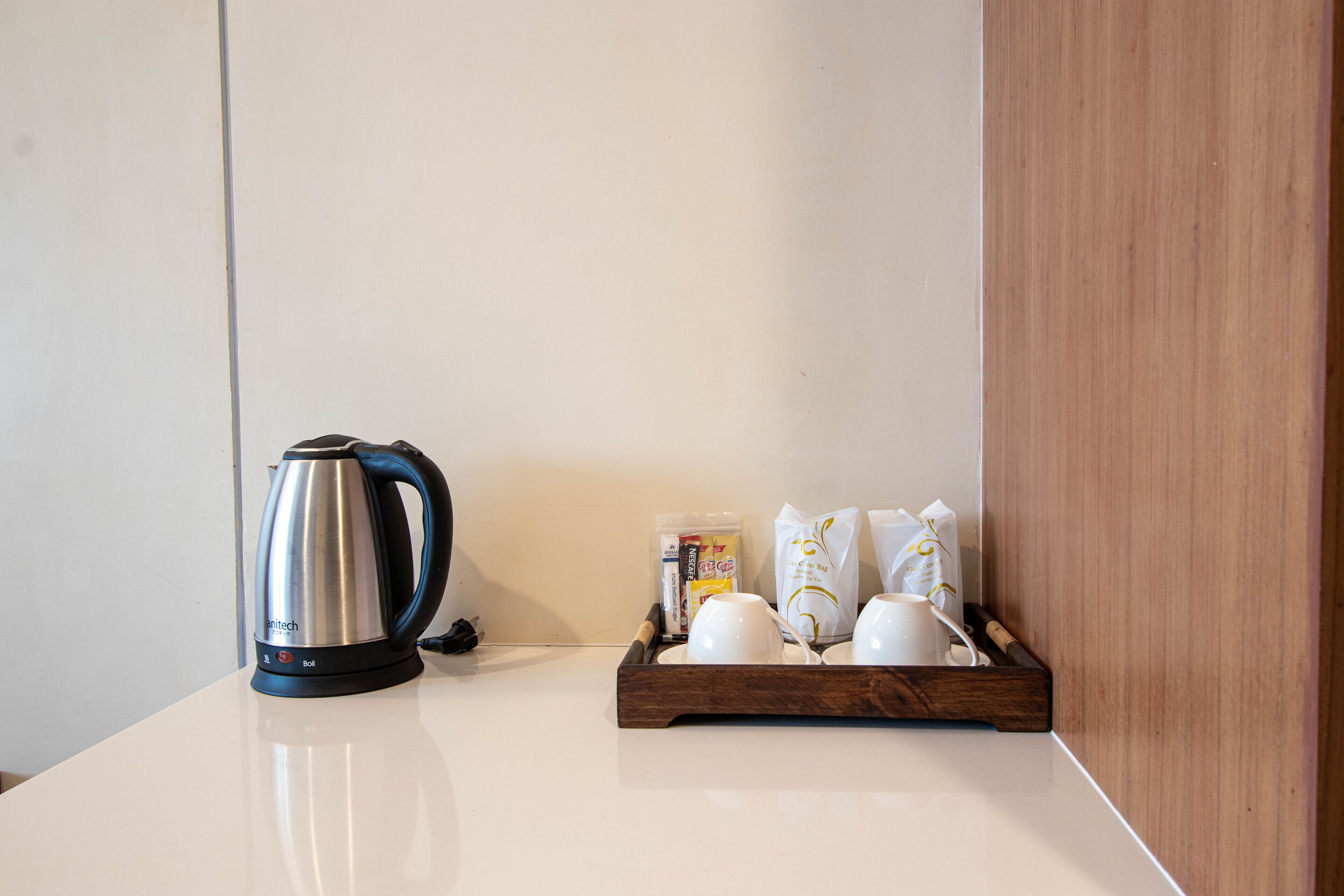 Een keukentafel met een waterkoker, een schotel met kopjes en verpakte etenswaren.