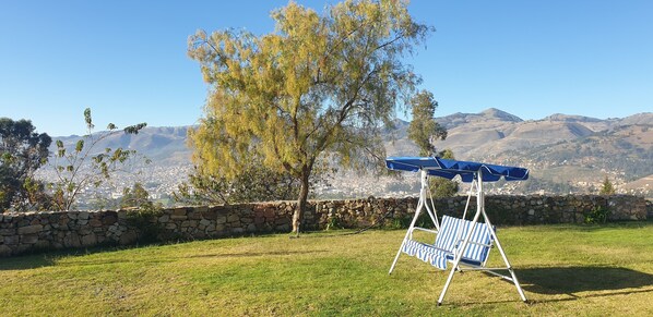 Un'area verde con prato, un muro in pietra e altalene con un ombrello blu.