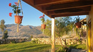A patio with hanging flower pots, a stone wall, and a view of a town and mountains in the background. - Ecolodge and Retreat "Casa de Colibri (Cajamarca)