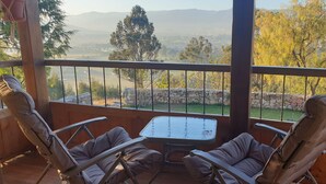 A balcony with two reclining chairs and a small table, overlooking a scenic landscape with trees and a stone wall. - Ecolodge and Retreat "Casa de Colibri (Cajamarca)