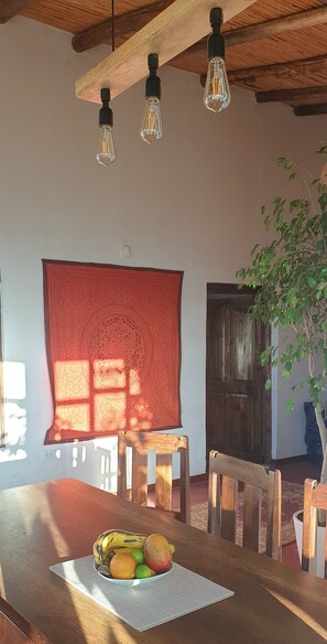 A dining area with a table set for a meal, featuring a potted plant and a tapestry on the wall.