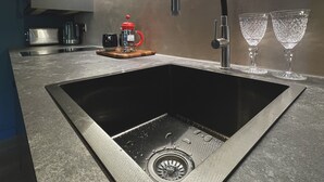 A modern kitchen with a stainless steel sink, a coffee machine, and two wine glasses on the counter.