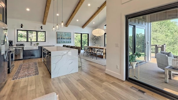 Une cuisine moderne dotée d’un îlot en marbre, de poutres en bois et de luminaires suspendus.