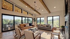 Un salon spacieux doté de grandes fenêtres, d’un plafond en bois et d’un lustre moderne.