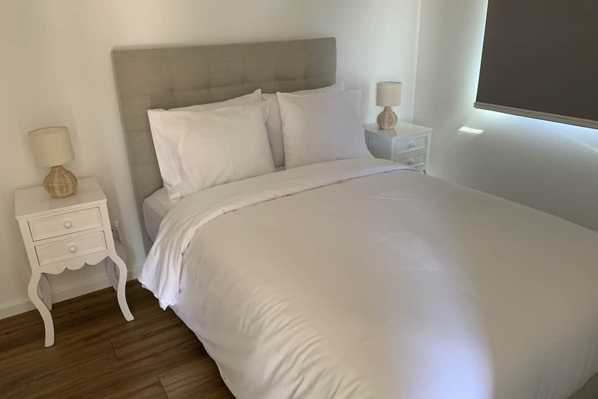 Un lit bien fait, avec une literie blanche, une tête de lit en bois et deux tables de chevet avec des lampes.