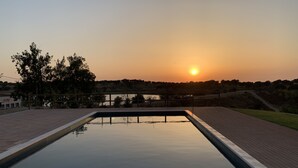 A swimming pool with a sunset view, surrounded by a wooden deck and trees.