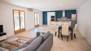 Un saló modern amb un sofà gris, una taula de dinar amb cadires i una zona de cuina amb armaris i electrodomèstics.